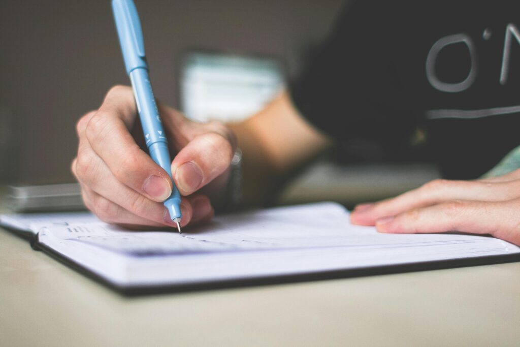 pexels-photo-210661-210661 Person Holding Blue Ballpoint Pen Writing in Notebook
